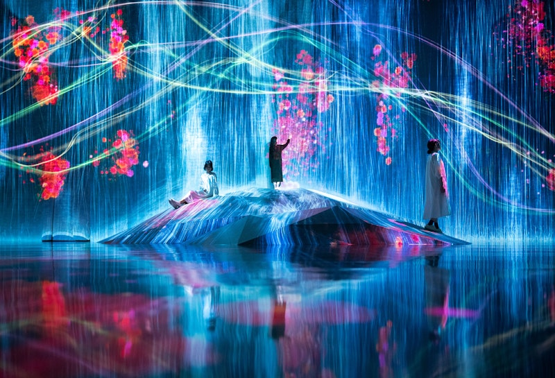 Drei Personen interagieren mit einer immersiven digitalen Kunstinstallation mit fließenden Wasserpartikeln und lebhaften Blumenprojektionen.