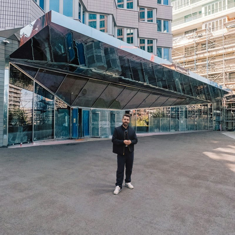 Hier ist die Übersetzung ins Englische:  Standard / Descriptive Translation Maximilian Pohlmann is standing in front of the media facade of the UBS Digital Art Museum.